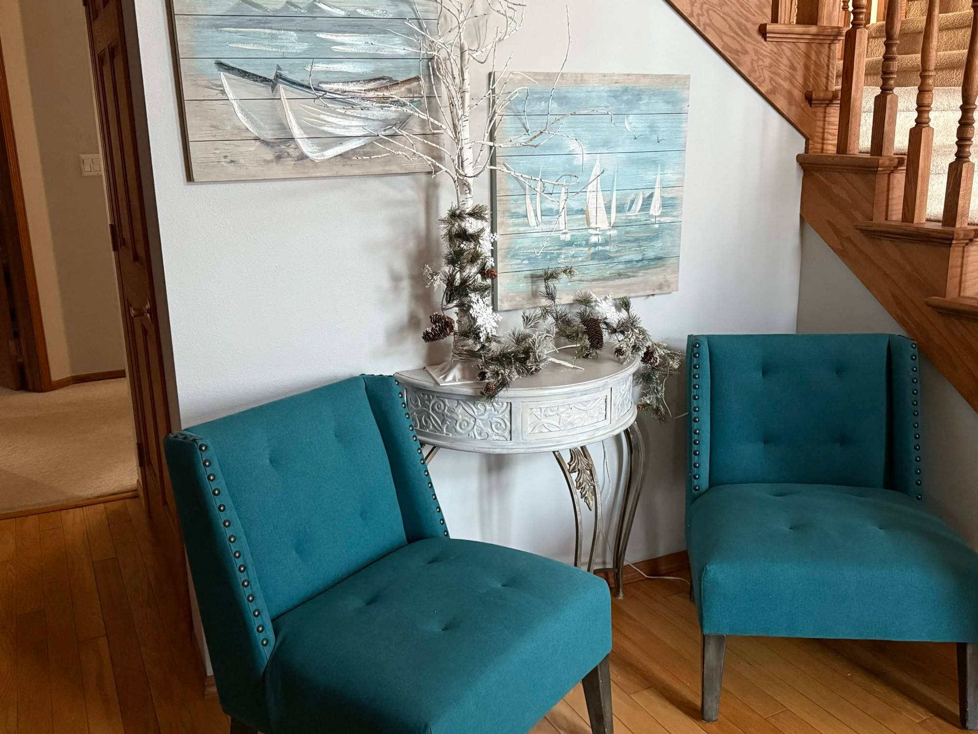 Two teal chairs beneath sailboat art by the stairs